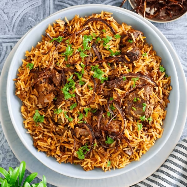 A light blue bowl filled with Indian biryani, garnished with fried onions and fresh cilantro.